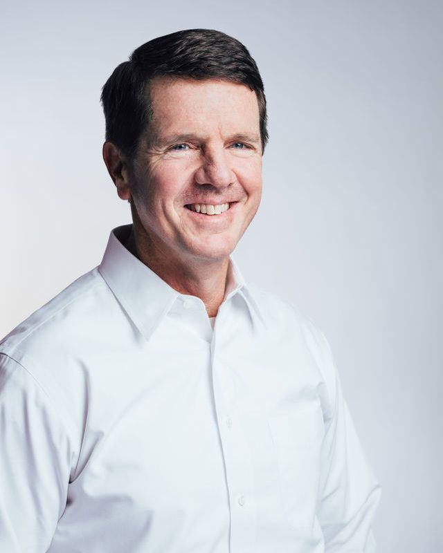 Hombre sonriente con camisa blanca sobre fondo gris claro