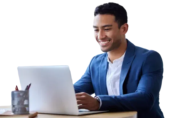 A man in a blue jacket is sitting at a desk using a laptop computer.