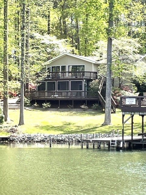 Cottage on a lake with a wooden dock and boathouse. Green trees surround the house.
