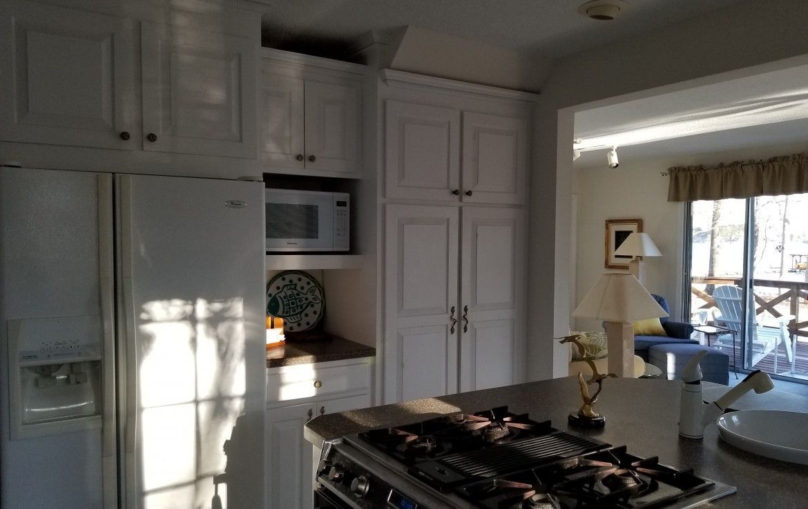 White kitchen cabinets, refrigerator, microwave, and range. View of living area in the background through an archway.