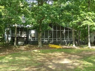 Cabin with a screened porch in a wooded area, surrounded by trees and grass.