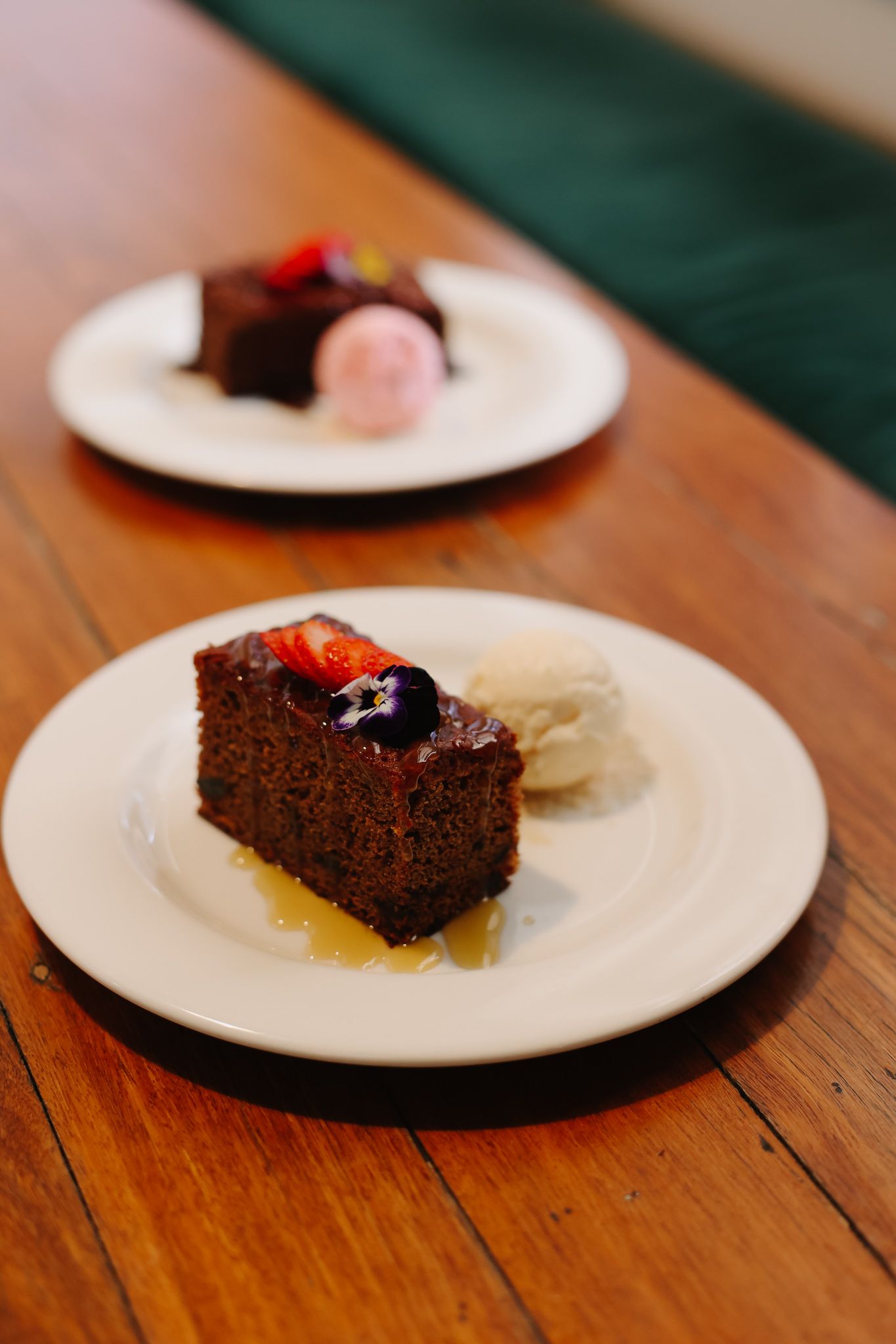 Two slices of chocolate cake with ice cream and fruit on white plates, on a wooden table.