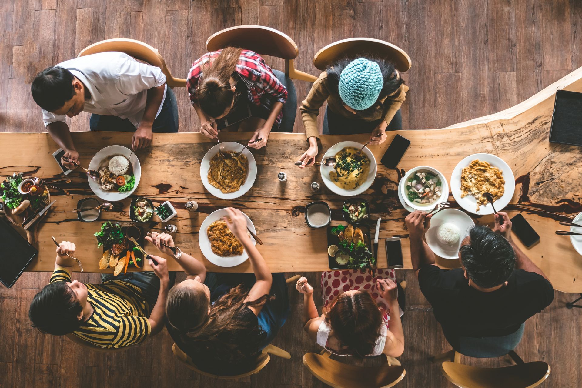People gathered around a long wooden table, sharing bowls of food in a top-down view.