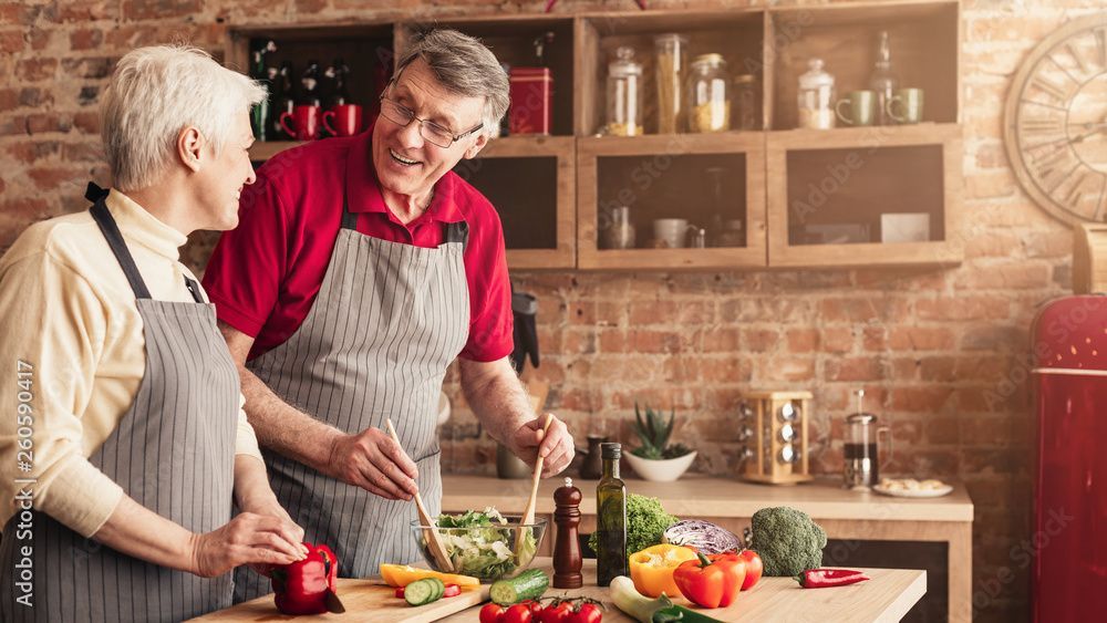 Two people in aprons smiling and chopping vegetables in a rustic kitchen with fresh produce on the counter