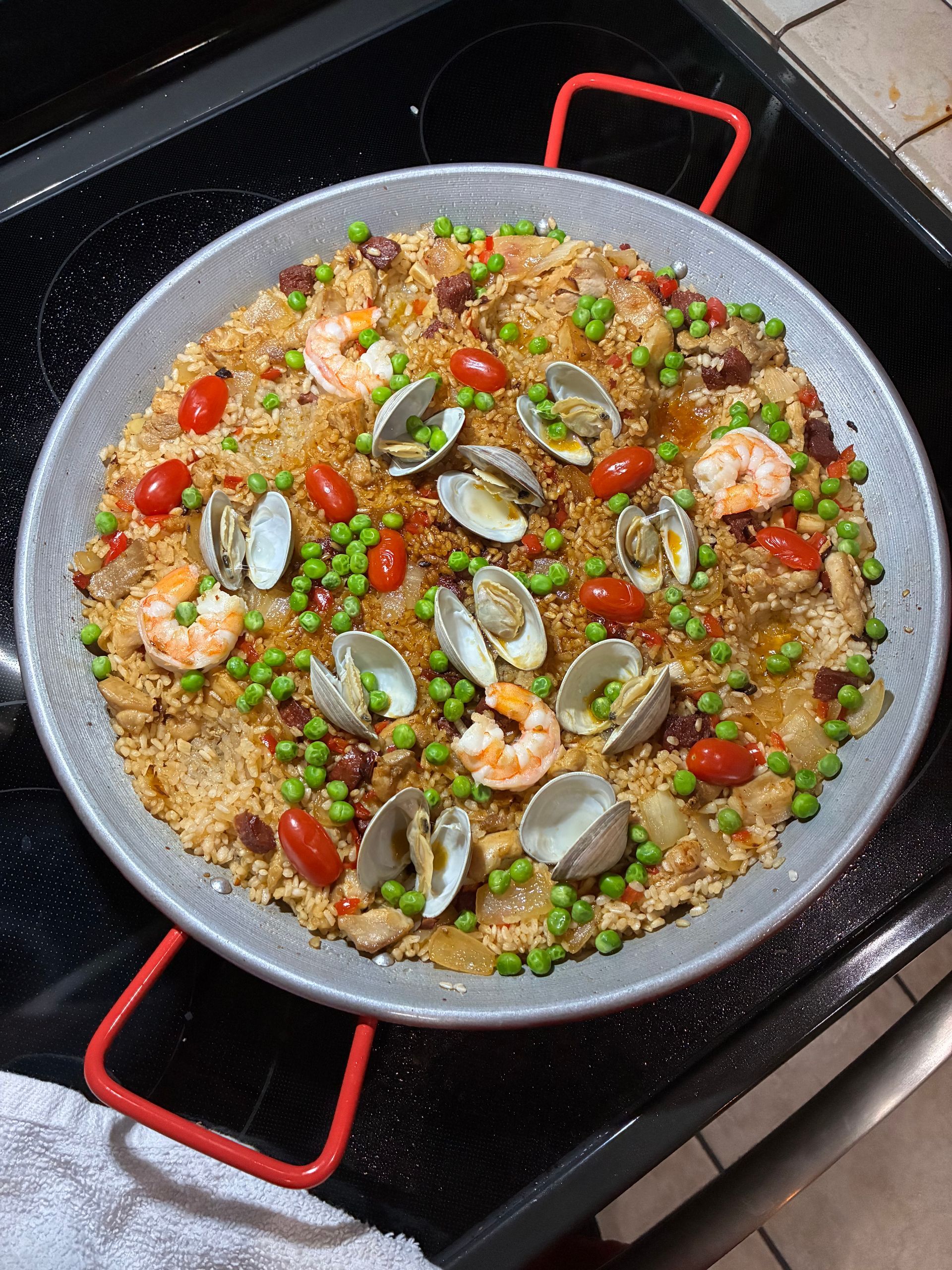 Seafood paella in a black pan, topped with clams, shrimp, peas, and red peppers