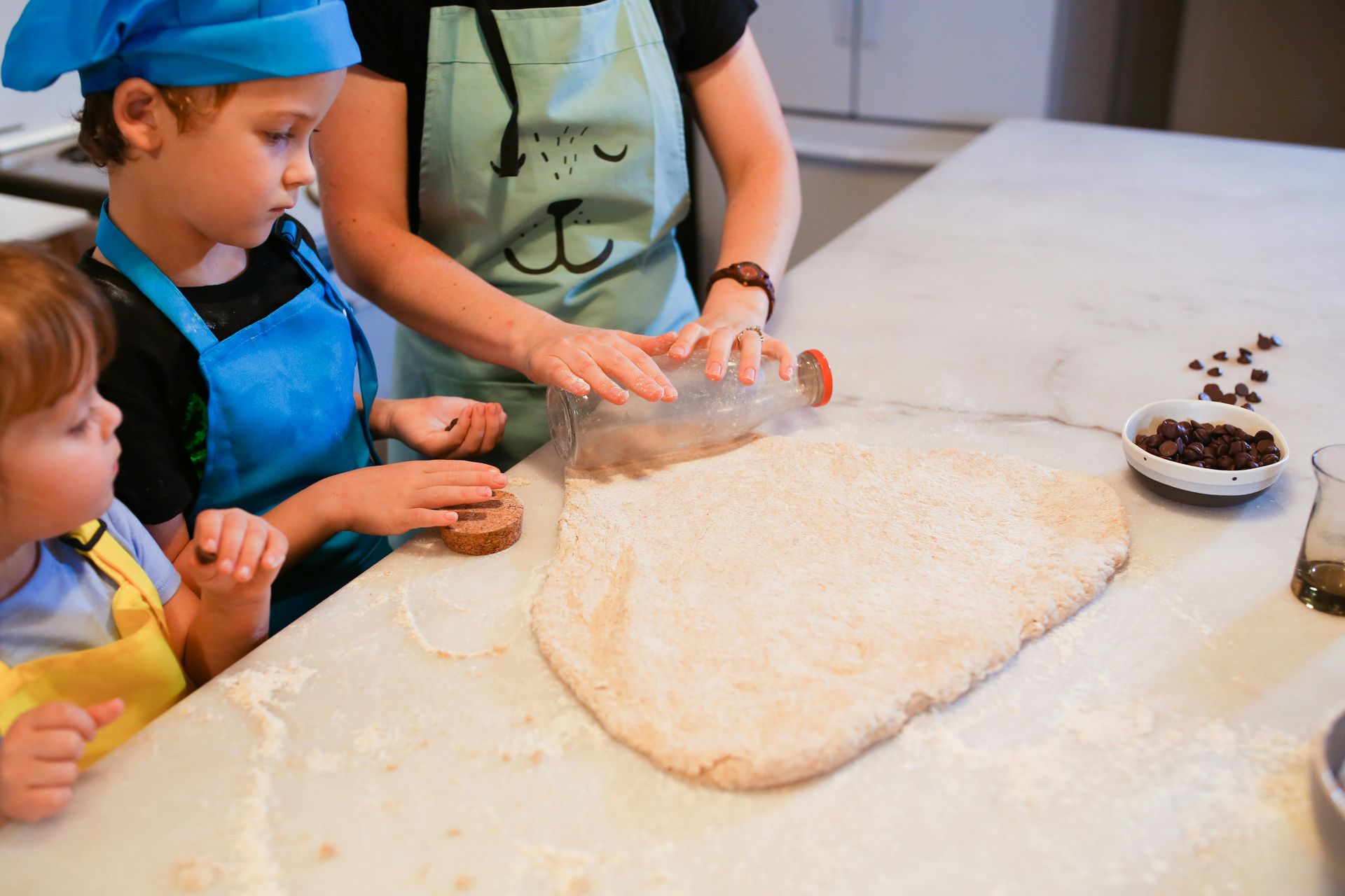 Children and an adult rolling dough on a flour-dusted kitchen counter