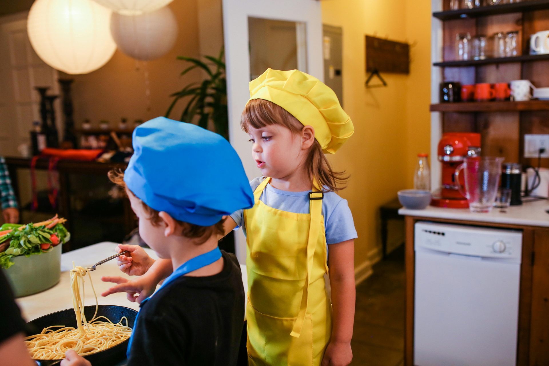 Two children in blue and yellow hats cooking in a kitchen