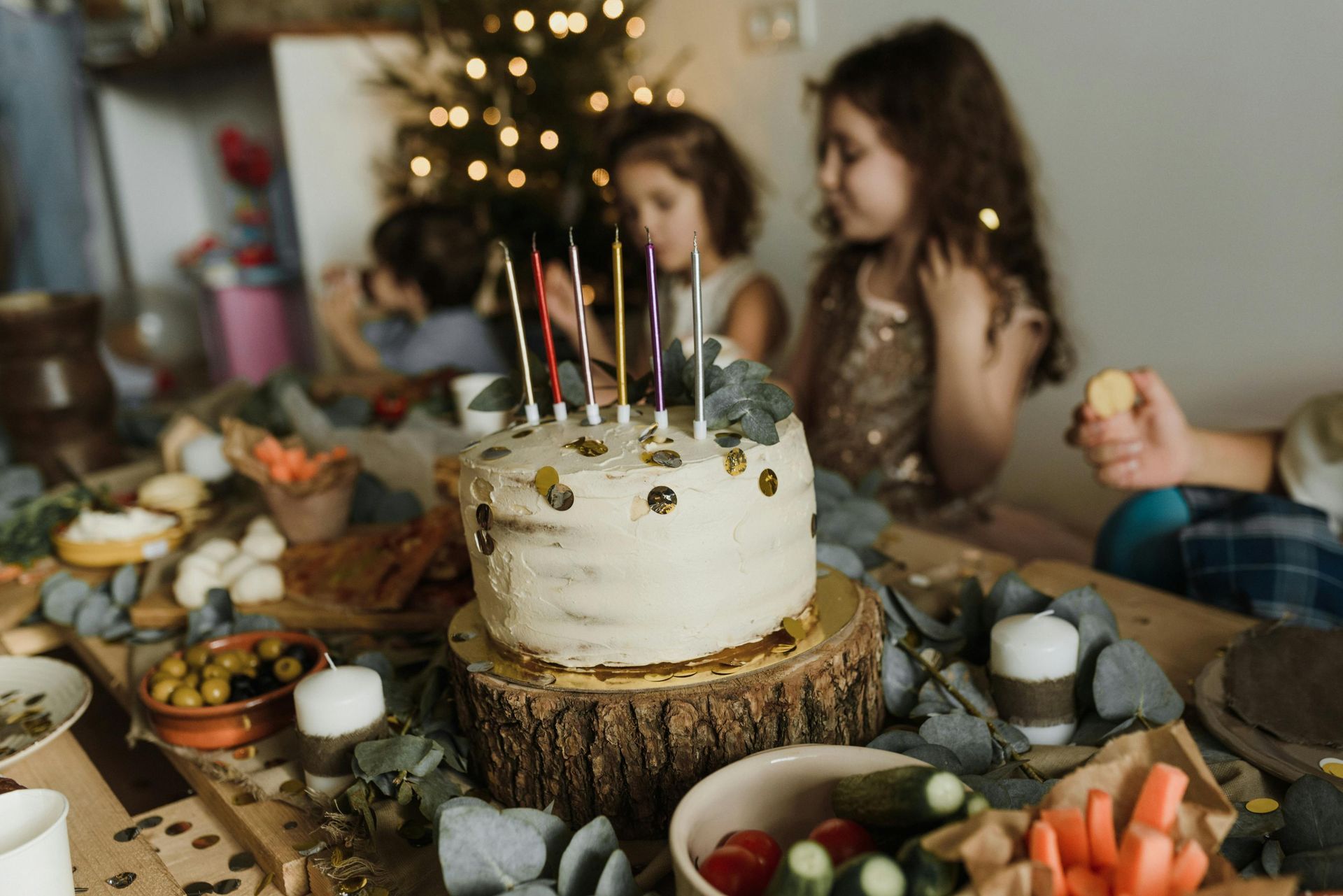 Candles on a rustic cake centerpiece at a decorated table, with two people seated in the background