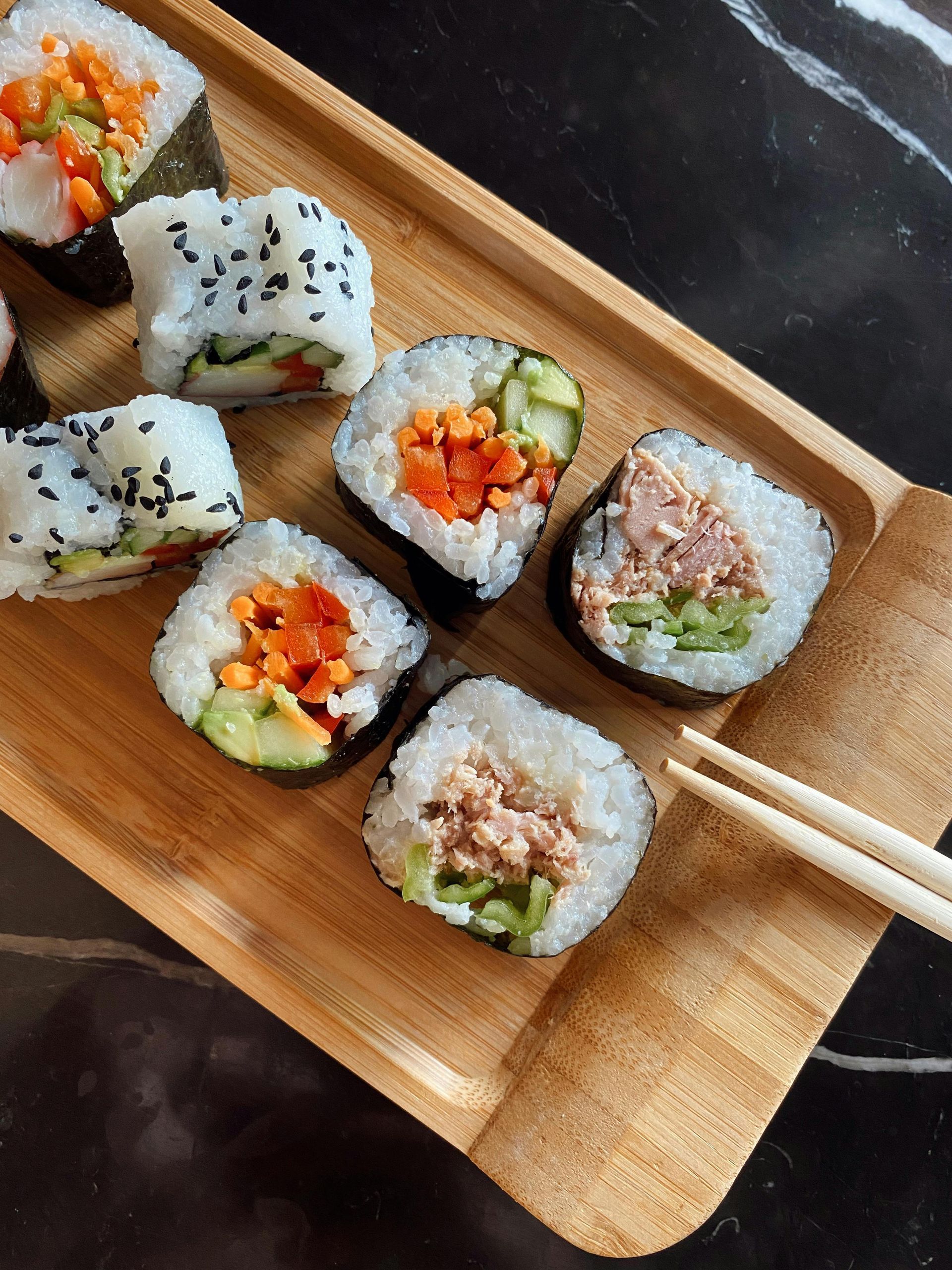 Sushi rolls on a wooden tray with chopsticks, showing colorful vegetable and fish fillings.
