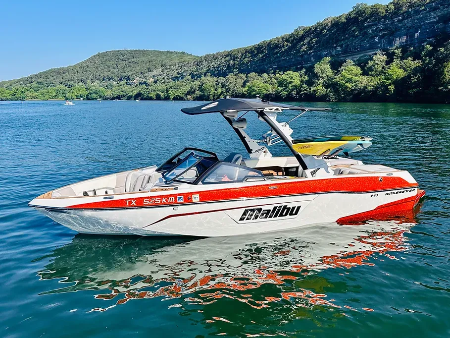 A red and white malibu boat is floating on a lake.