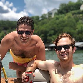 Two shirtless men are standing next to each other on a boat.