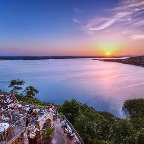 A group of people are sitting on a balcony overlooking a large body of water at sunset.