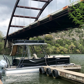 A pontoon boat is docked under a bridge on a lake.