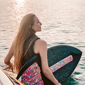 A woman is sitting on a boat holding a surfboard in the water.