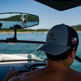 A man wearing a hat is driving a boat in the water.
