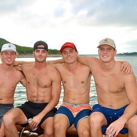 A group of shirtless men are sitting on a boat in the water.