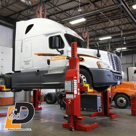 A white semi-truck raised on red hydraulic lifts inside a service bay.