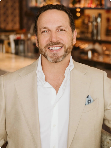 Dan Simons sharp dressed khaki suit standing in front of a bar