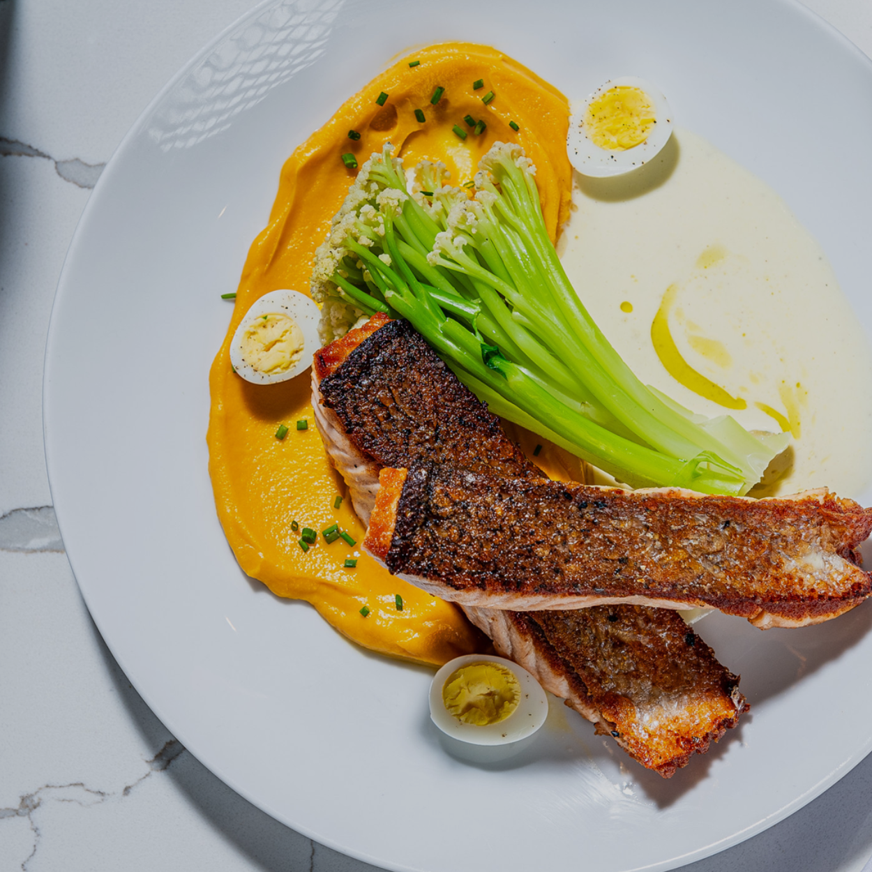 Client: Maison Cheryl - Seared Salmon on orange purée with green asparagus and halved quail eggs on a white plate