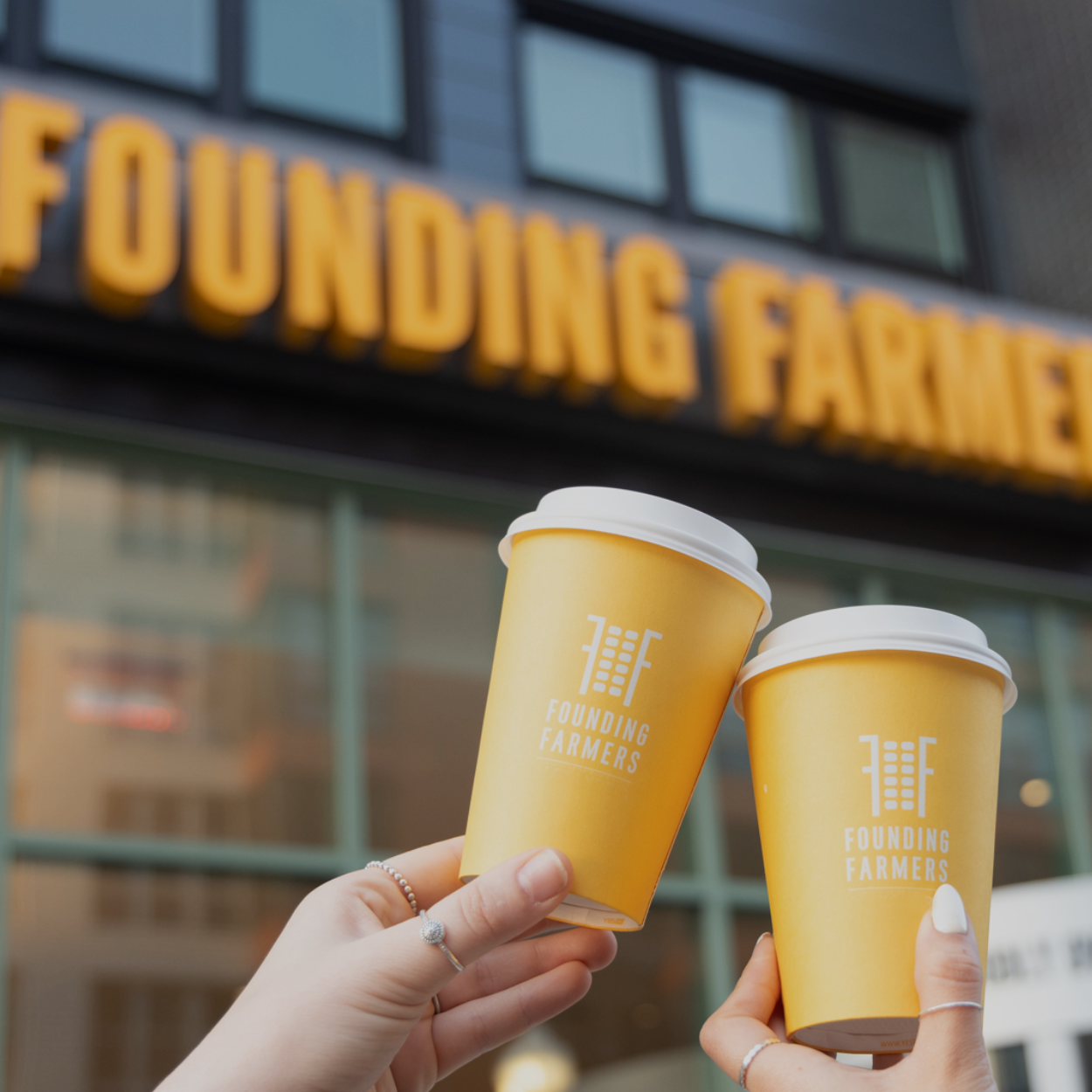 Client Founding Farmers - Two people holding coffees in front of Founding Farmers