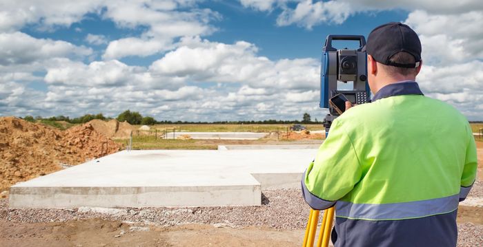 Worker in neon jacket watching a construction site with a concrete slab and heavy machinery under a cloudy sky