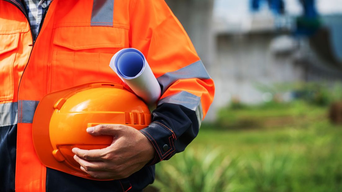 Construction worker holding an orange hard hat and rolled blueprints outdoors