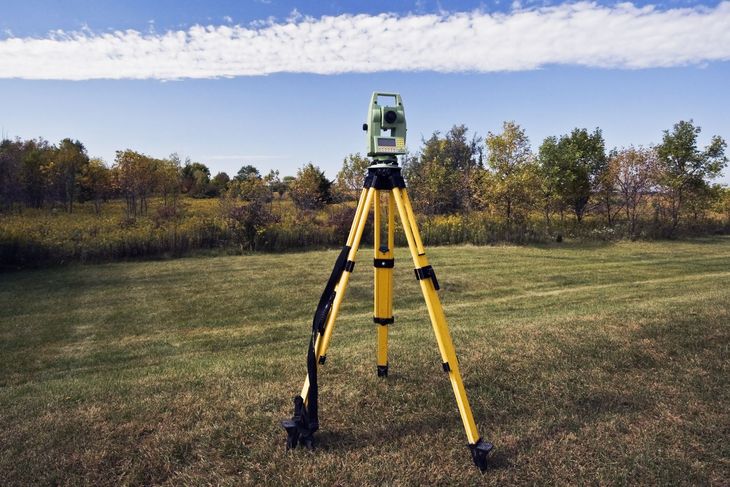 Surveying tripod on a grassy field under a blue sky