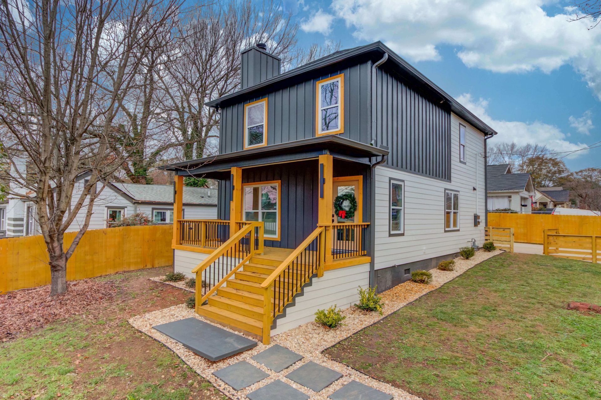 A two-story house with dark vertical siding, light-colored lower walls, and a prominent yellow porch and staircase.