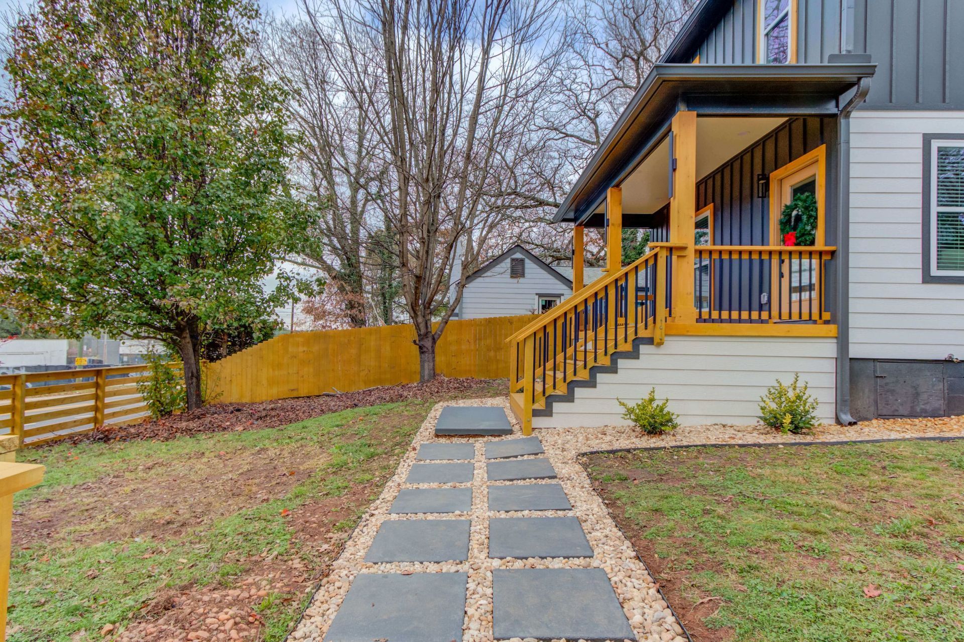 A grey house with a yellow porch and railing, featuring a stone paver walkway leading to the front steps.