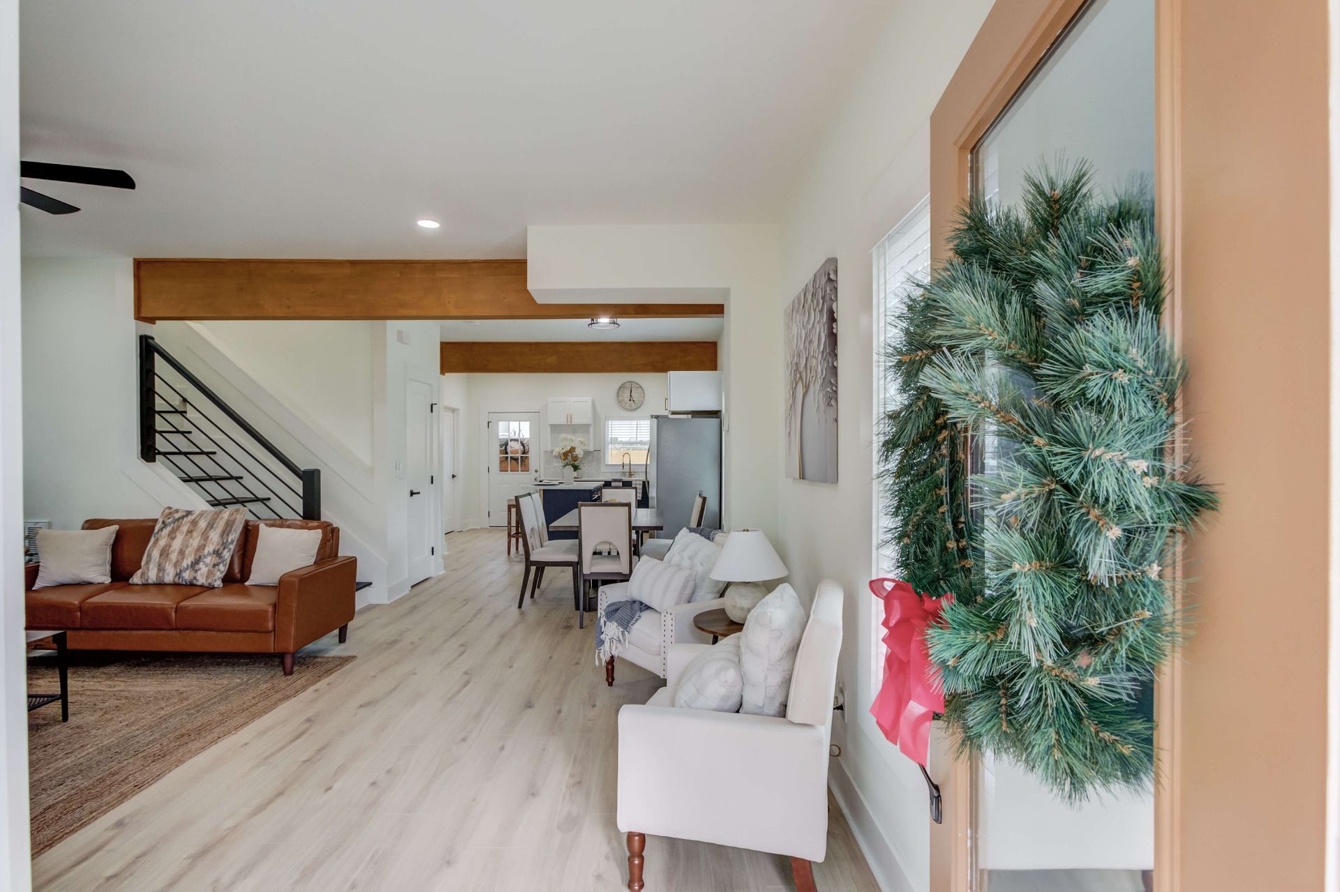 View from an entryway with a wreath-decorated door into an open-plan home featuring a brown sofa, chairs, and dining area.