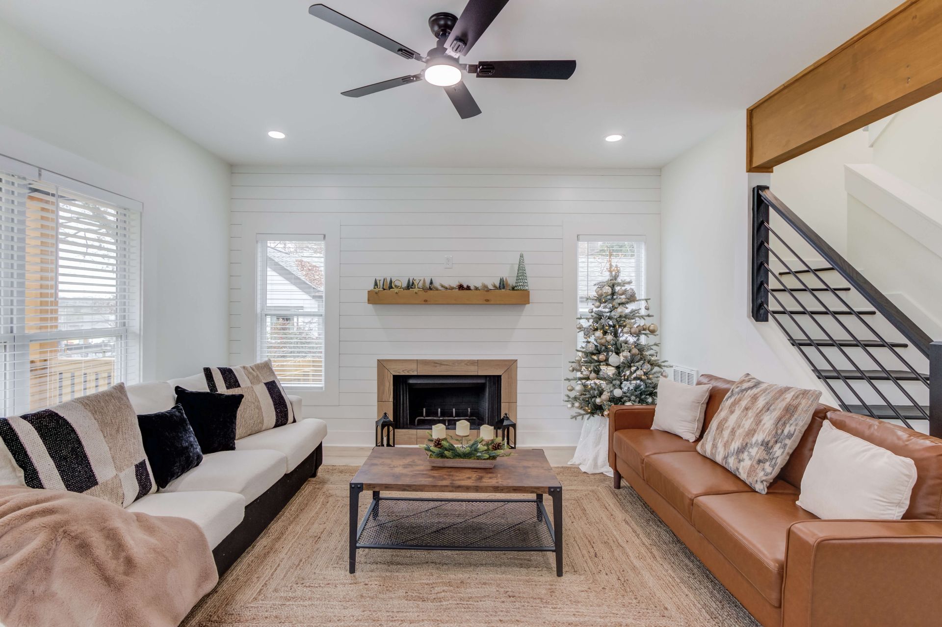 Modern living room with a white shiplap fireplace, two sofas, a coffee table, and a staircase with a black metal railing.