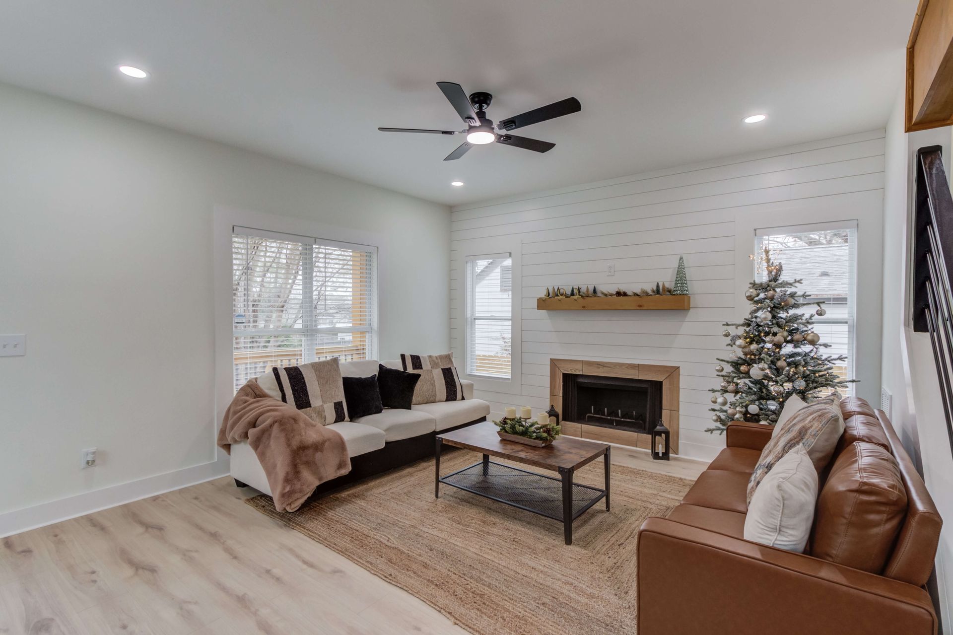 Living room with a white fireplace, a light-colored sofa with throw blankets, a leather couch, and a Christmas tree.