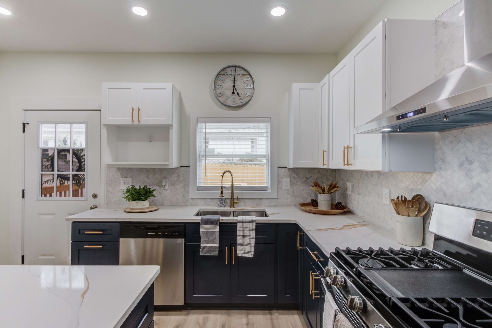 A modern kitchen with dark blue lower cabinets, white upper cabinets, a stainless steel range, and a quartz island.