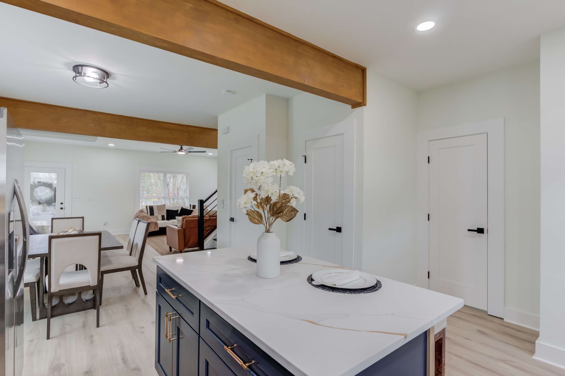 Modern kitchen with a dark blue island, white countertops, and a dining area visible in the background.