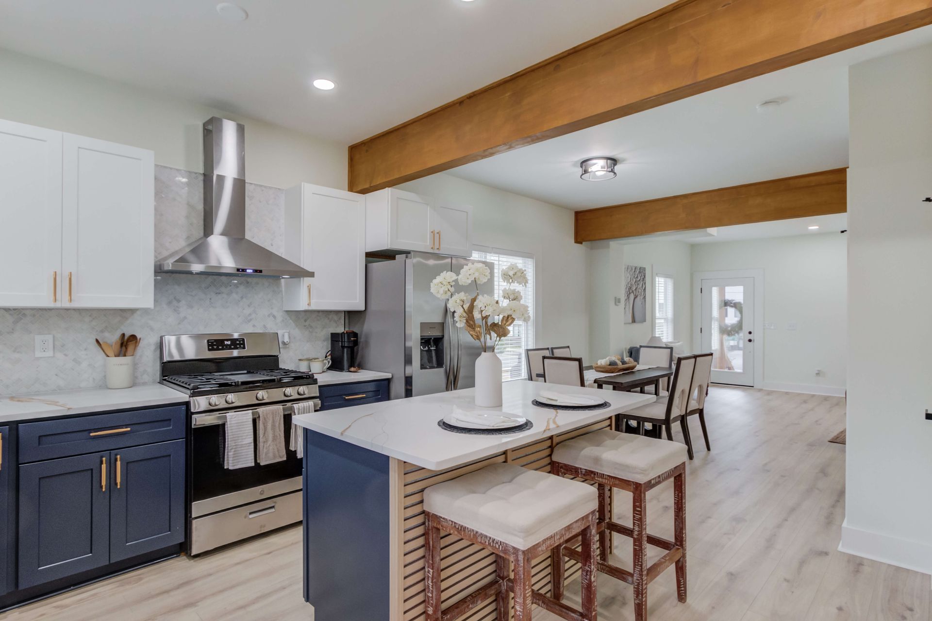A modern kitchen with blue lower cabinets, white upper cabinets, a stainless steel range, and a central island with seats.