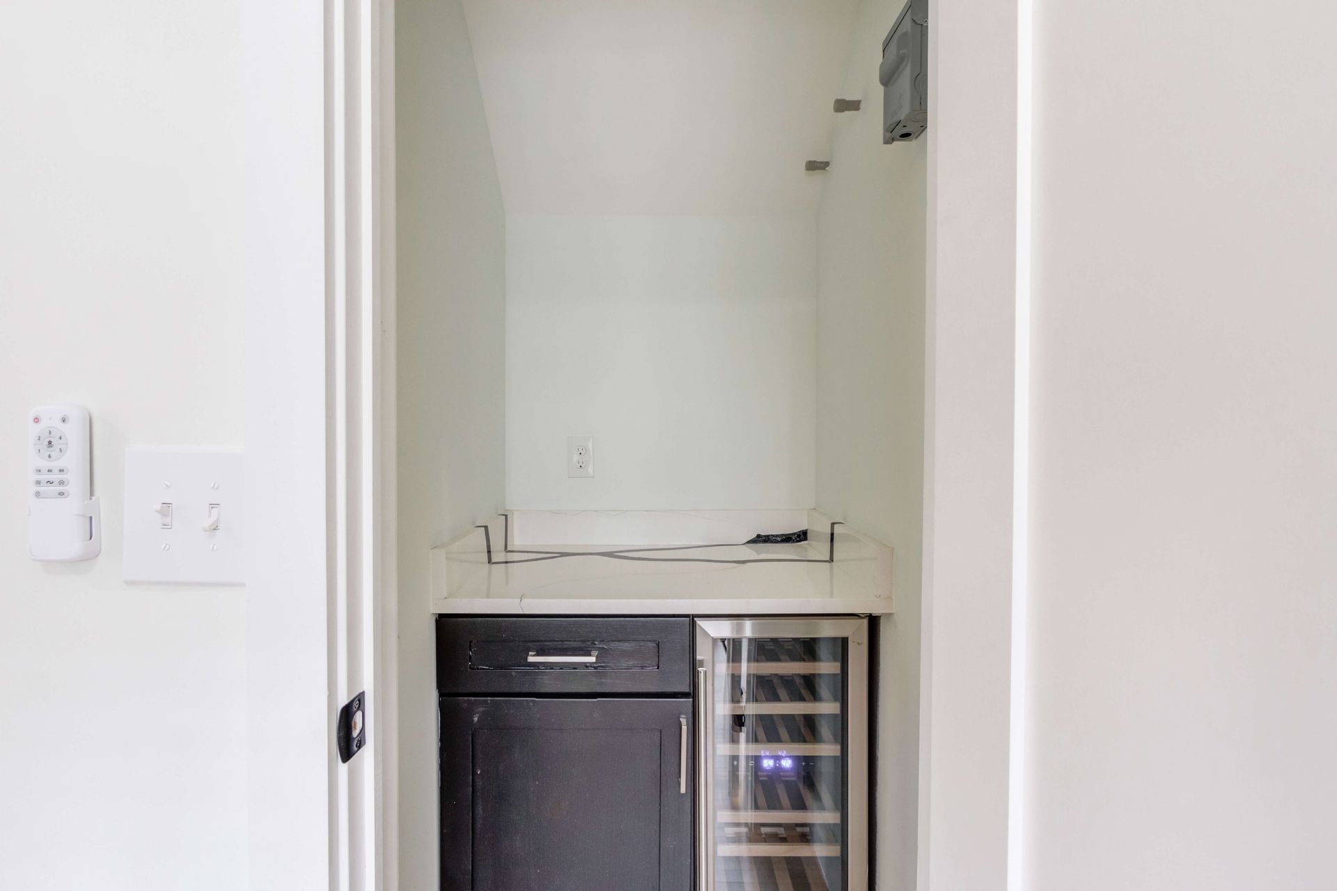 A built-in bar nook with white walls, a dark wood cabinet, and a glass-front wine refrigerator.