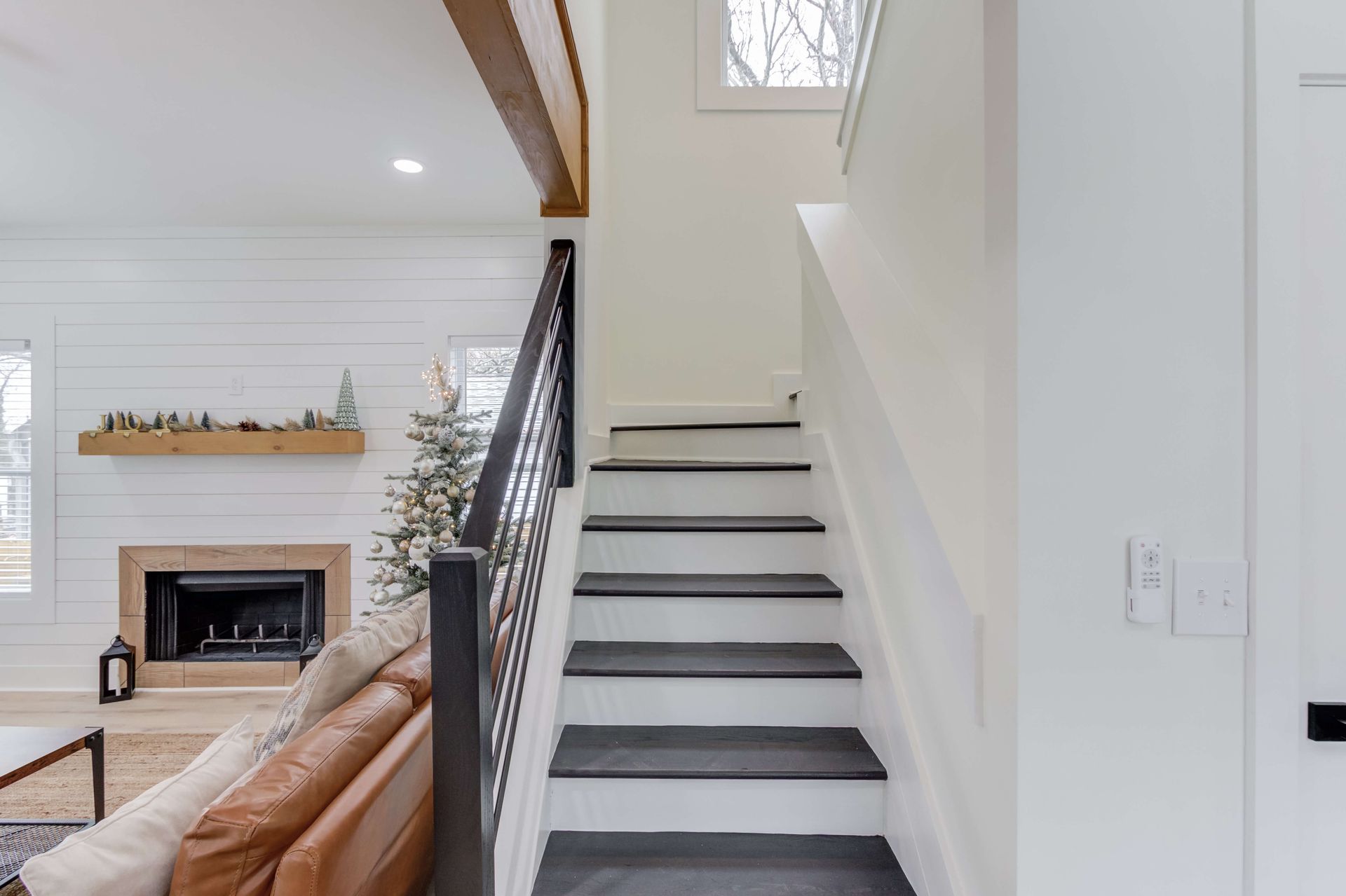 A modern staircase with white risers and dark treads, next to a living room with a fireplace and white shiplap walls.