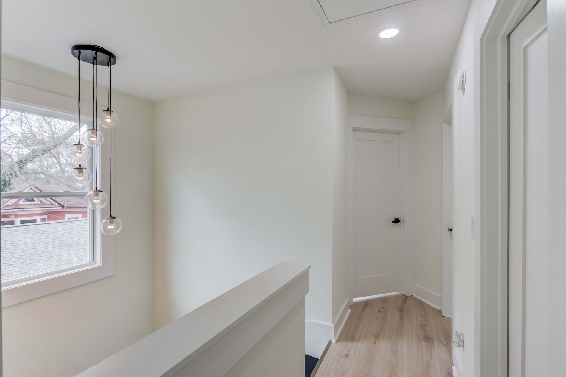 A modern hallway with light wood flooring, white walls, two closed doors, and a multi-bulb pendant light fixture.