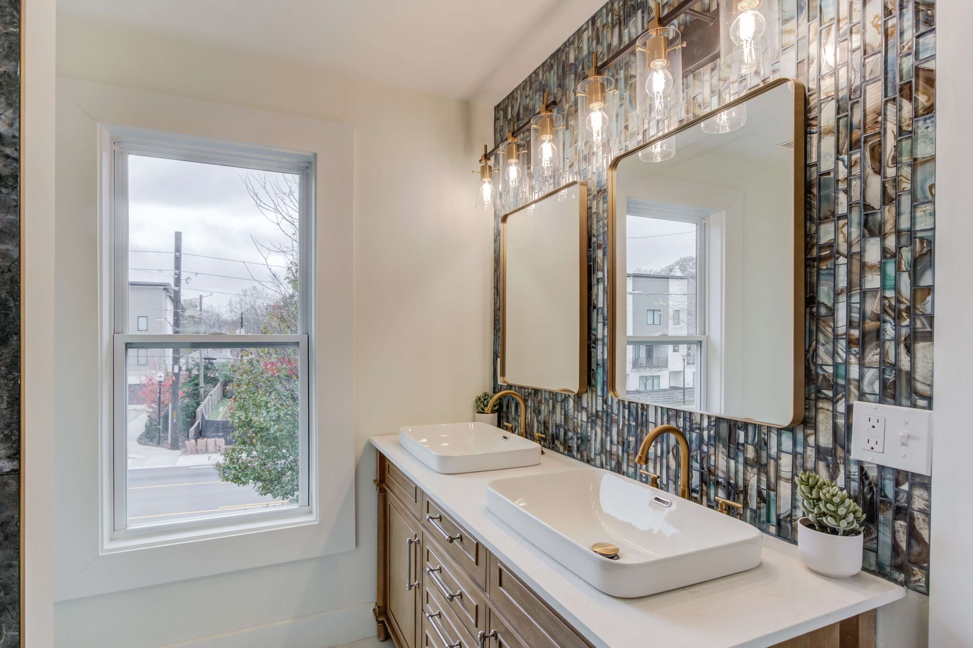 A bathroom vanity with two white vessel sinks, gold faucets, rectangular mirrors, and a decorative tile accent wall.