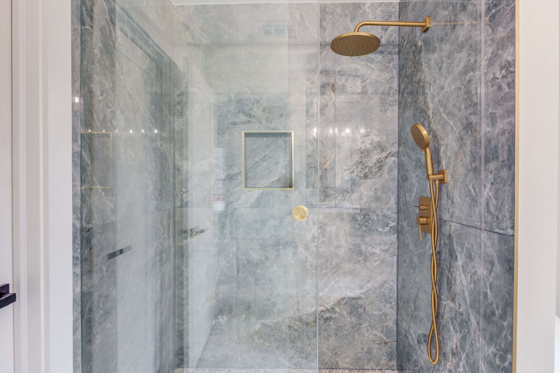 A walk-in shower with grey marble-patterned tiles and gold-toned shower fixtures.