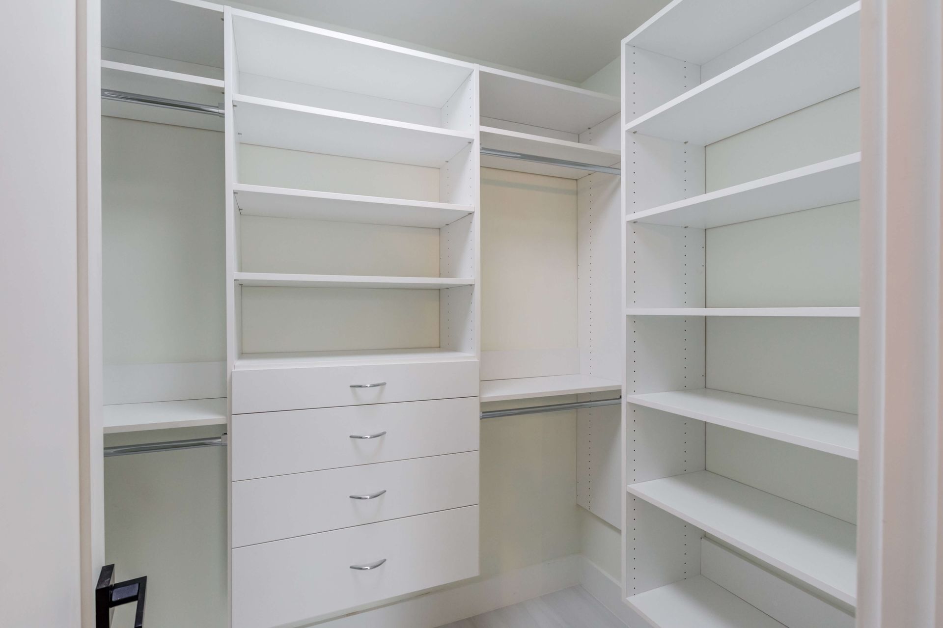 A white walk-in closet featuring built-in shelving, hanging rods, and a central column of four drawers.