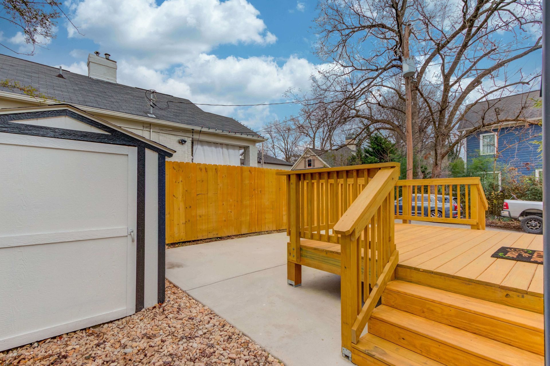 A wooden deck with stairs leads to a backyard with a shed, a concrete patio, and a yellow wooden privacy fence.