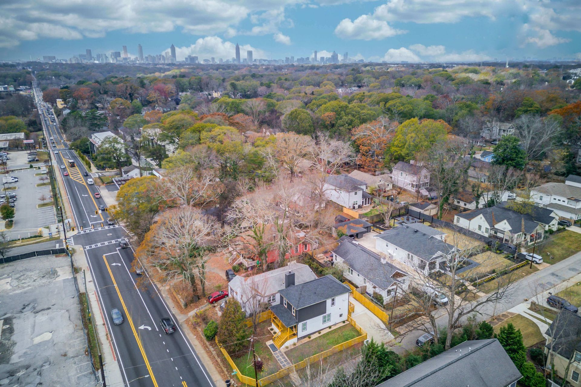 Aerial view of a residential neighborhood with houses near a road and a city skyline visible in the distance.