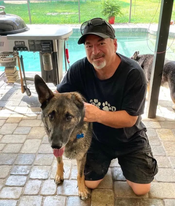 A man kneeling down with a dog in front of a pool
