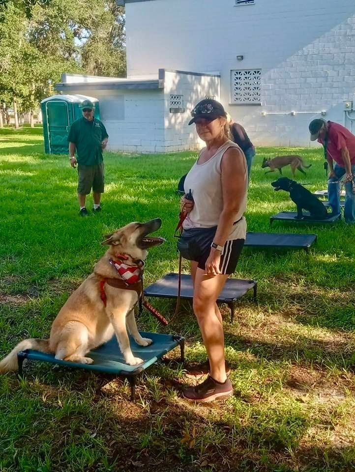 A woman is standing next to a dog on a bed in a park.
