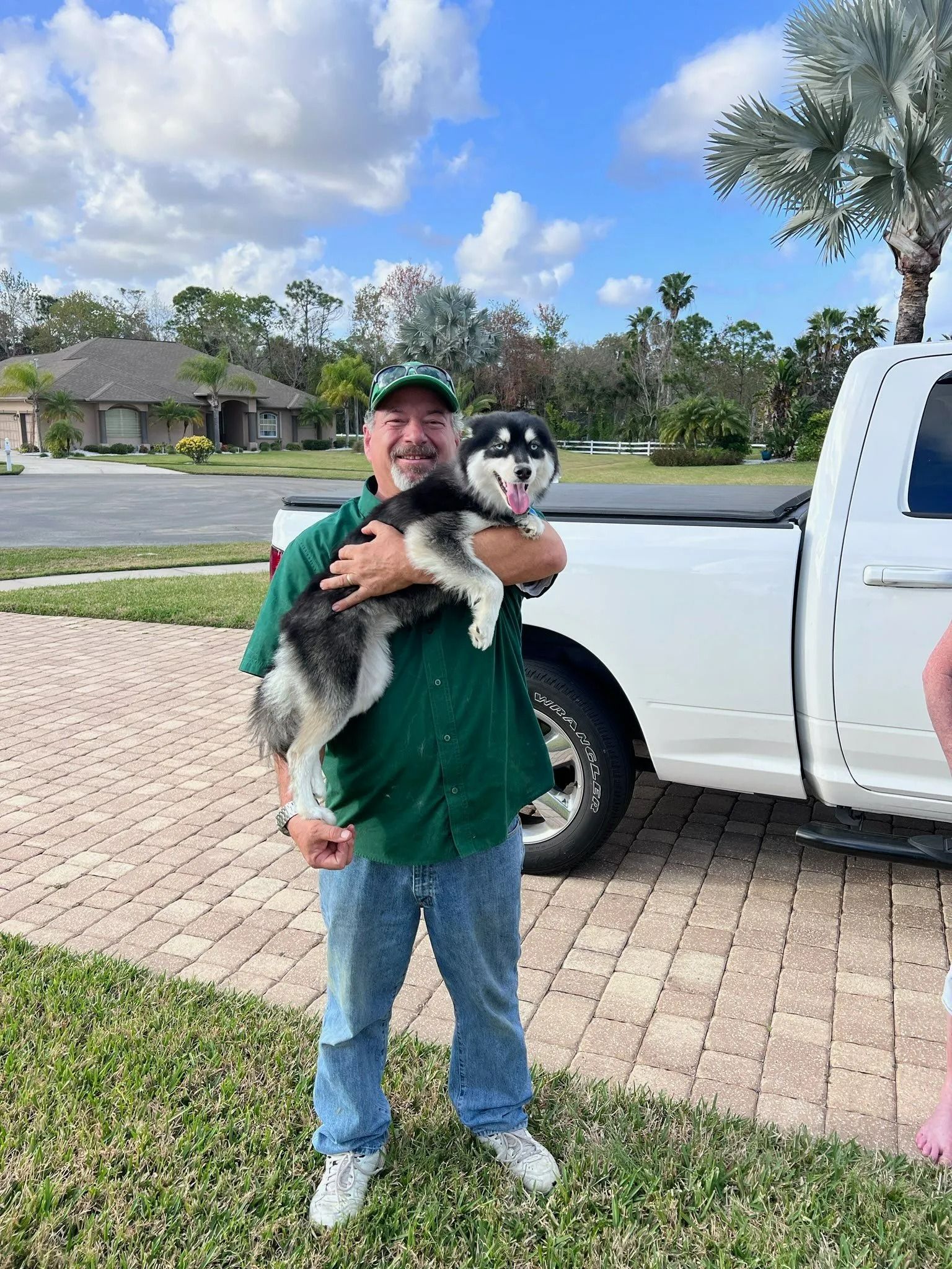 A man is holding a husky puppy in front of a white truck.
