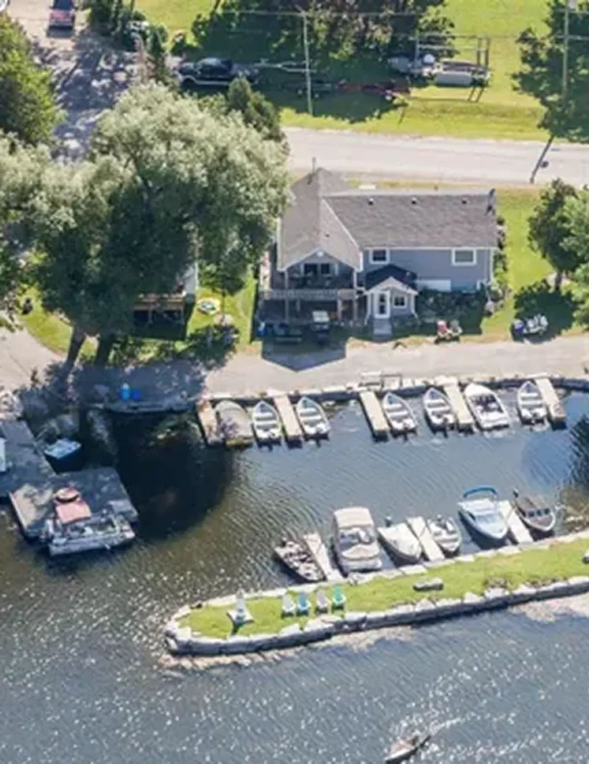 Aerial view of a waterfront home with boats docked along the shore and a road behind it.