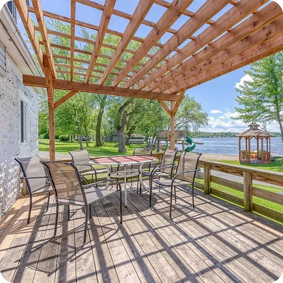 Wooden deck with pergola and patio furniture overlooking a lake on a sunny day