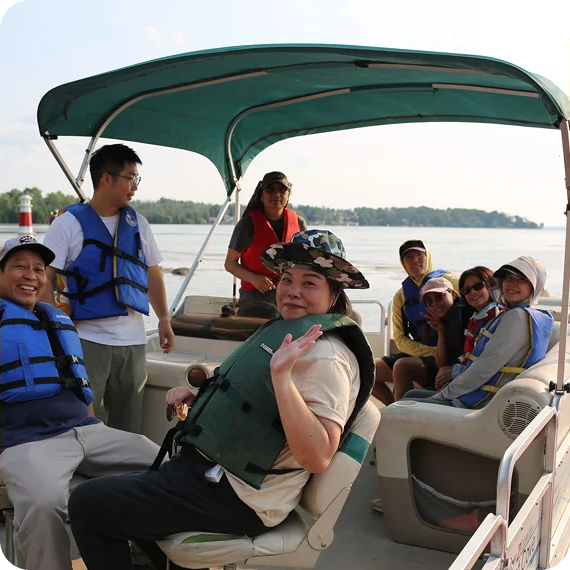Group seated on a covered boat, wearing life vests on calm water under bright daylight