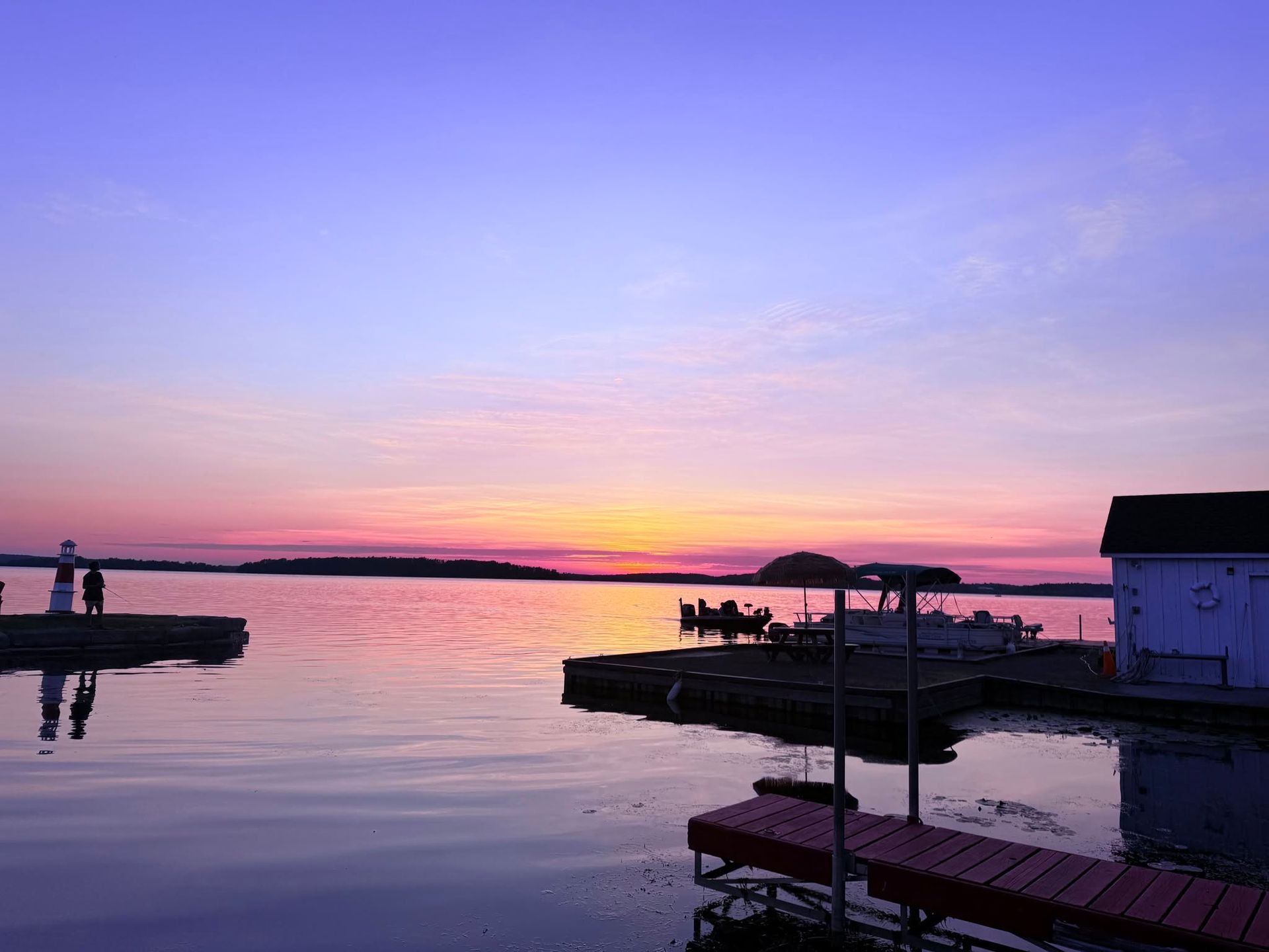 Sunset over a calm harbor with pink and purple sky, silhouetted docks, and boats moored near shore